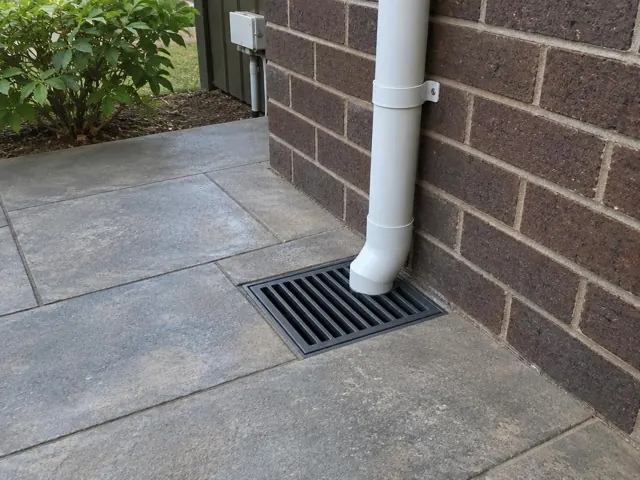 Paved area beside a brick wall with a seated stormwater grate and downpipe in Castle Hill
